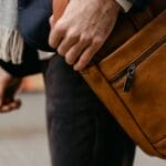 A fashionable man carrying a brown leather bag hints at modern business travel.