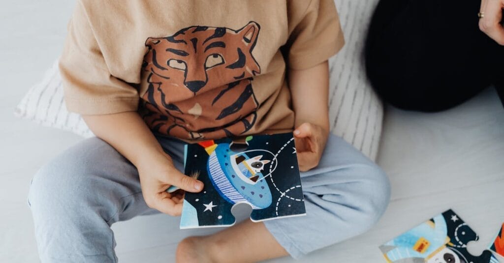 A young child sits on the floor assembling a space-themed puzzle piece.