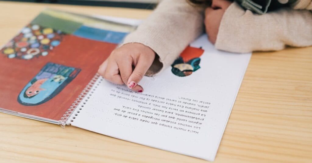 Child's hand pointing at illustrations in a colorful book on a wooden table.