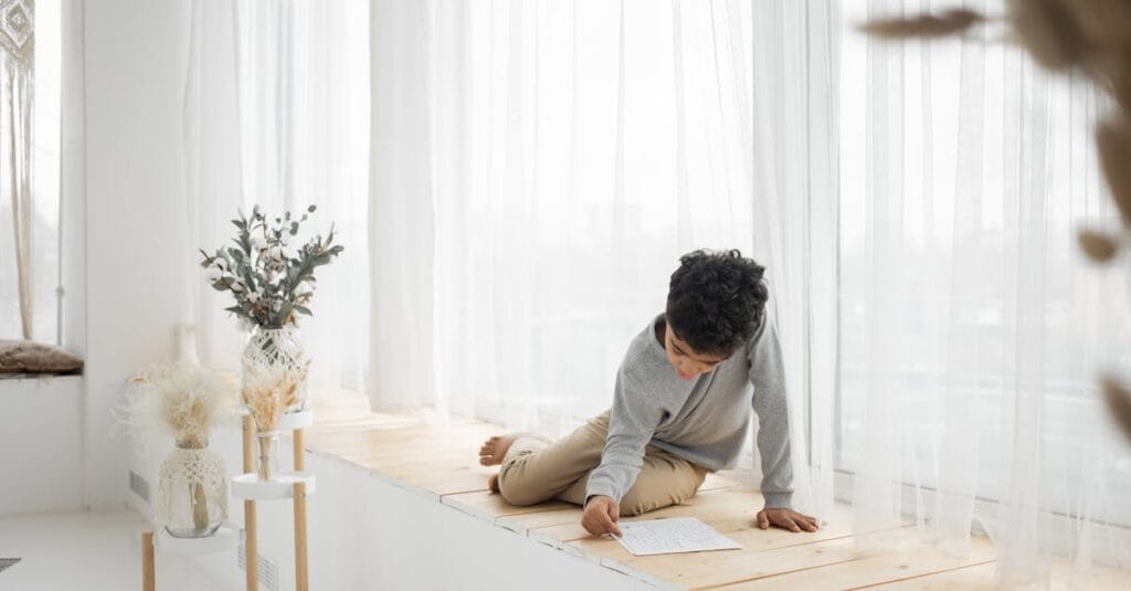 Boy solving a puzzle on a sunlit windowsill, enjoying a quiet moment indoors.