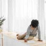 Boy solving a puzzle on a sunlit windowsill, enjoying a quiet moment indoors.