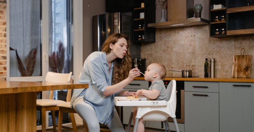 A mother lovingly feeds her baby in a modern kitchen setting.