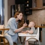 A mother lovingly feeds her baby in a modern kitchen setting.