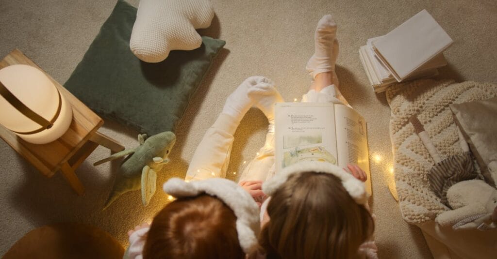 Two children in pajamas reading a book together at bedtime with soft lighting and toys around.