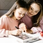 A mother and daughter collaborate on a school project at the kitchen table, fostering learning and creativity.