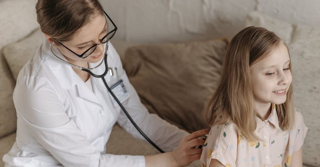 A doctor with a stethoscope examining a smiling girl during a medical check-up at home.