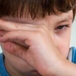 Close-up portrait of a young boy wiping away tears, expressing emotion.