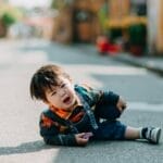 A child sitting on an empty street, expressing sadness and frustration.