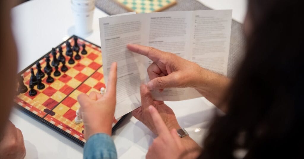 Adult and child reading chess instructions while setting up a chess game.