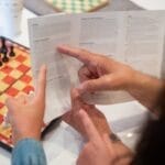 Adult and child reading chess instructions while setting up a chess game.