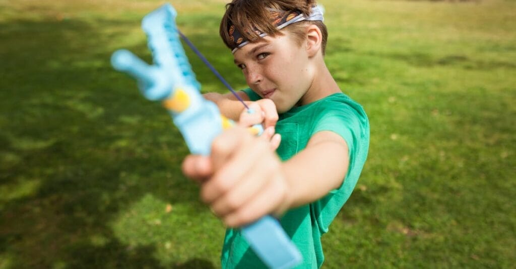 A boy in a park aiming a slingshot, showing playful outdoor activity.