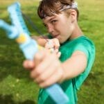 A boy in a park aiming a slingshot, showing playful outdoor activity.