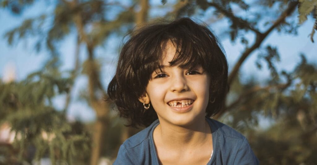 Joyful child smiling brightly in a sunny outdoor setting, surrounded by nature.