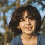 Joyful child smiling brightly in a sunny outdoor setting, surrounded by nature.