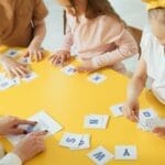 Group of children engaging with alphabet cards on a bright yellow table for learning.