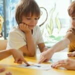 Young children engaging in fun learning activities at a yellow table in a classroom setting.