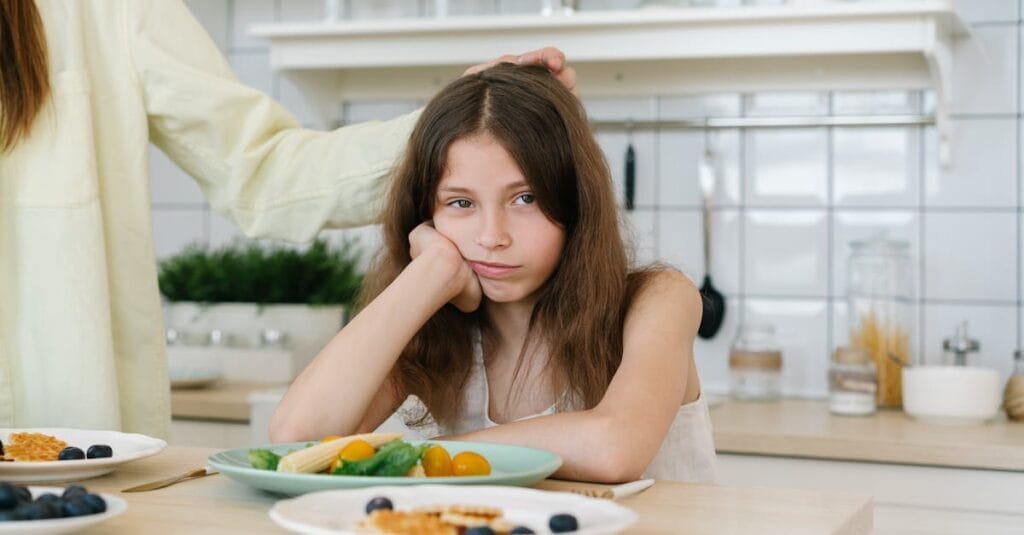 Young girl looking displeased with breakfast in a home kitchen setting.