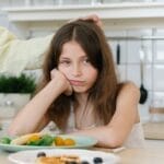 Young girl looking displeased with breakfast in a home kitchen setting.