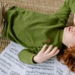 A child lying on a rug surrounded by music sheets, expressing frustration.