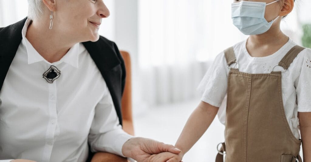 An adult and a child sharing a warm moment indoors, holding hands and smiling.