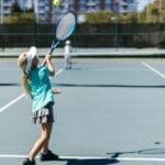 A girl in sportswear hitting a tennis ball on a sunny outdoor court.