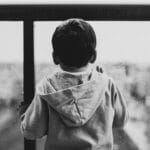 A young boy in a hoodie looks out a rainy window, creating a moody black-and-white scene.