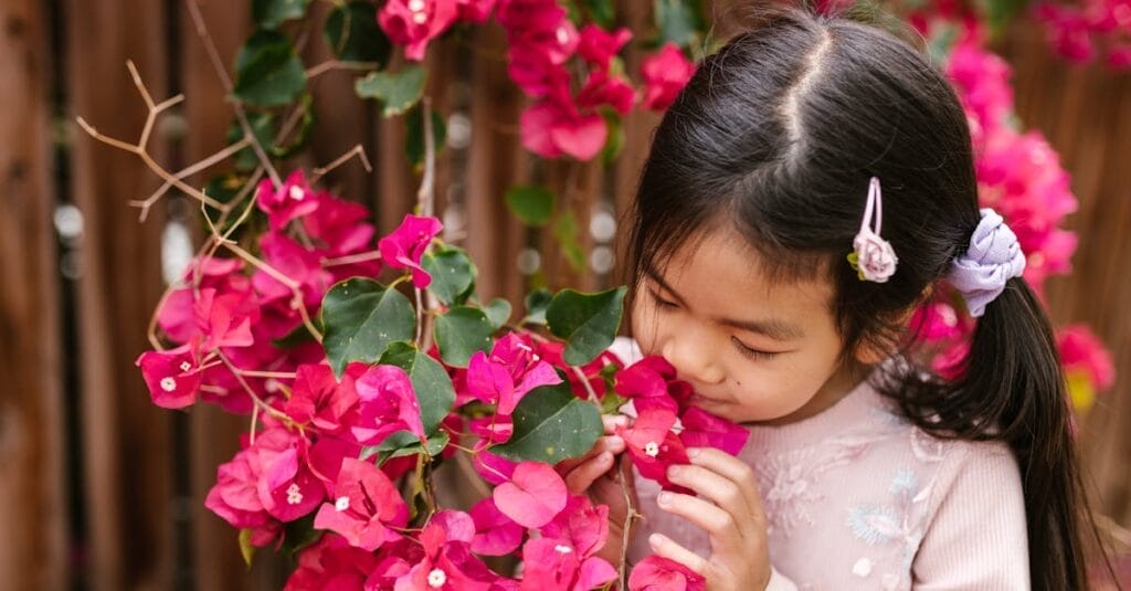 A young girl enjoys the beauty of vibrant pink bougainvillea blossoms outdoors.