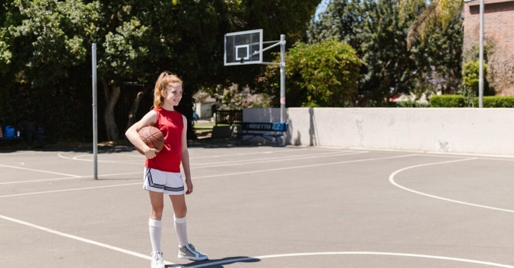 A young girl holding a basketball on an outdoor court, enjoying a sunny day.