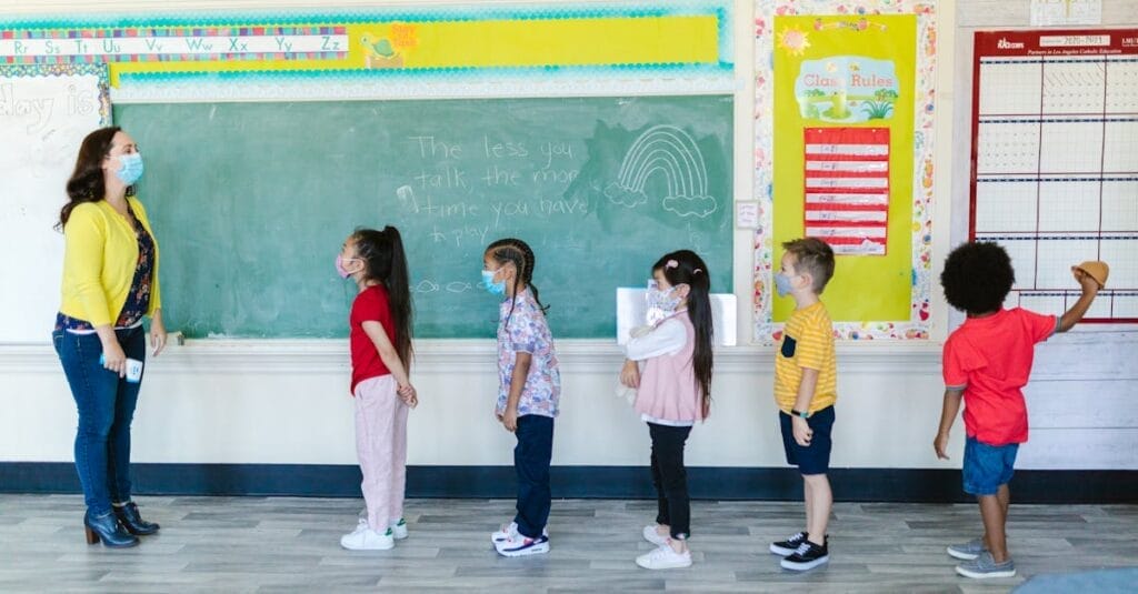 Teacher and diverse children wearing masks in line for classroom activity, embracing new normal.