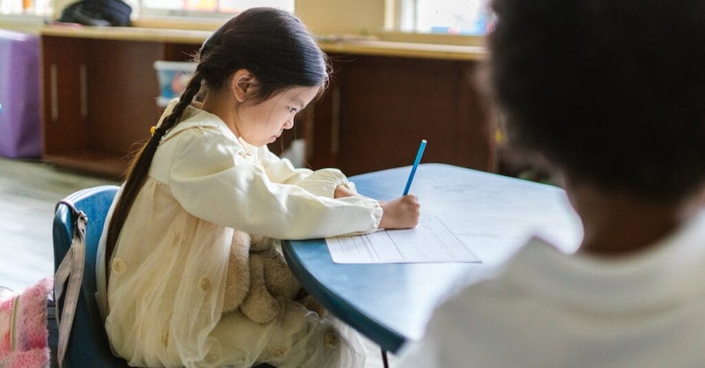 A young child intensely focused on writing at a classroom table, showing concentration and learning.