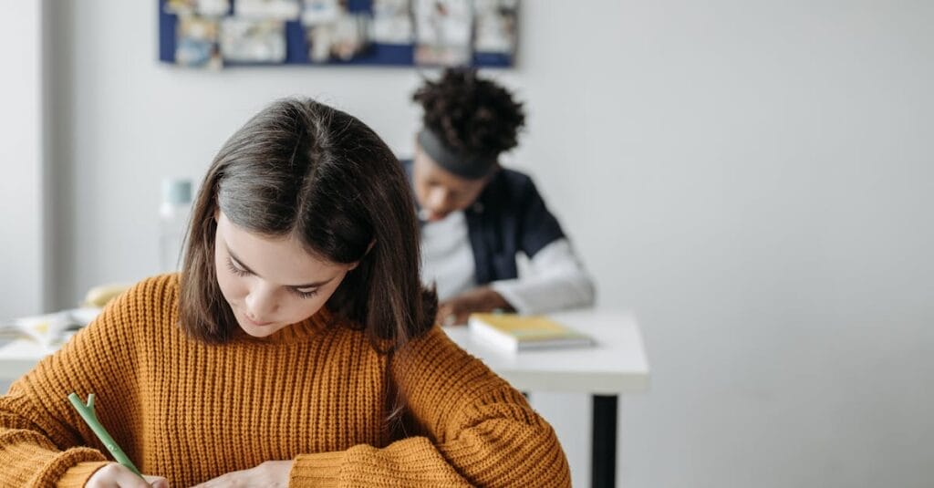 Two students concentrated on writing during class in a bright classroom setting.