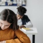 Two students concentrated on writing during class in a bright classroom setting.