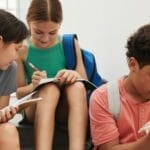 Children of diverse backgrounds studying together, writing in notebooks indoors.