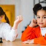 Two young girls engaged in a playful chess game indoors, showcasing focus and friendship.