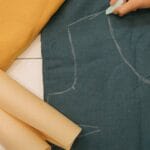 Top view of hands drawing sewing pattern on fabric with chalk and paper