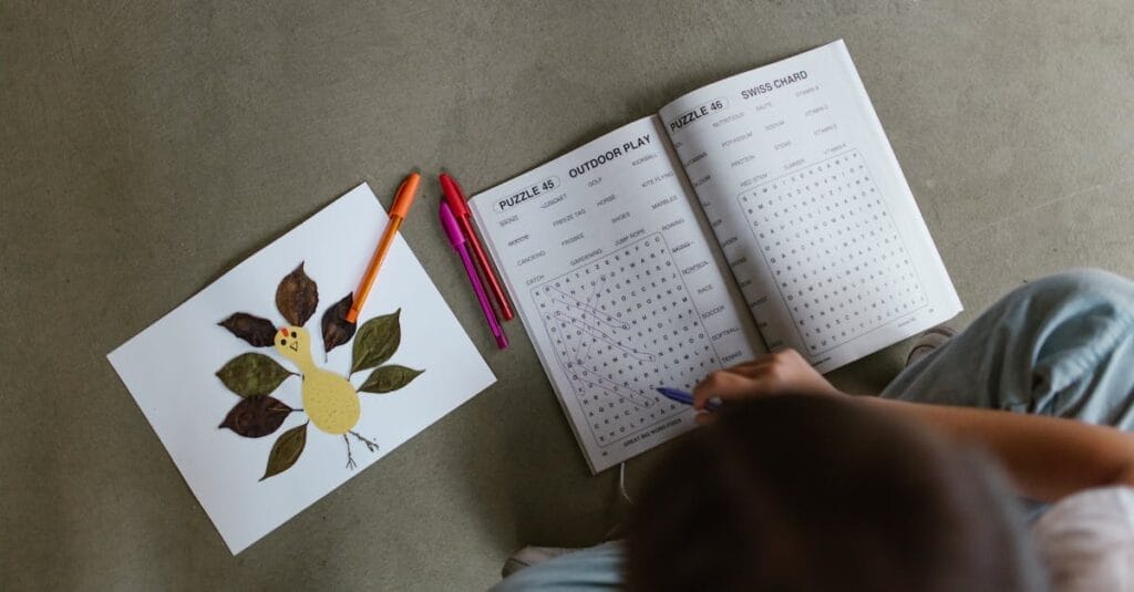 Top view of child engaged in a word puzzle, next to a handmade leaf art.