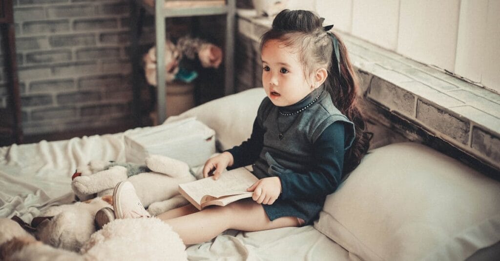 A cute little girl reading a book in a warm and cozy bedroom environment.