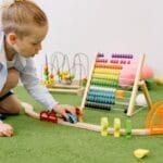 Young child playing with colorful educational toys indoors on a green carpet.