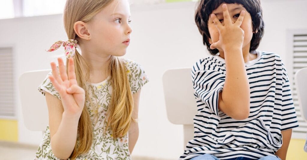 Two children sitting indoors engaging in a playful learning activity, showing numbers with fingers.