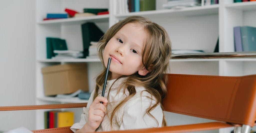 Adorable girl posing with a pencil in a modern home office setting, showcasing creativity and thoughtfulness.