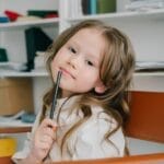 Adorable girl posing with a pencil in a modern home office setting, showcasing creativity and thoughtfulness.