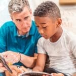 Father and son studying together at home, focused on learning with a tablet and notebook.