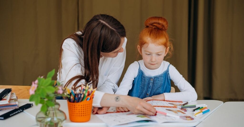 Teacher helps young girl with learning activity in a classroom setting, fostering education.