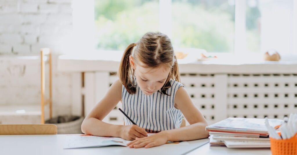 A young girl engaged in coloring at a desk indoors. Bright natural lighting.