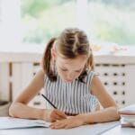 A young girl engaged in coloring at a desk indoors. Bright natural lighting.