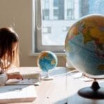 A young girl diligently studying in a sunlit classroom with a globe and books.