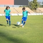 Children playing football on a sunny day in a Portuguese stadium.