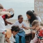 A group of children volunteering to clean a beach with a 'Save the Earth' sign.