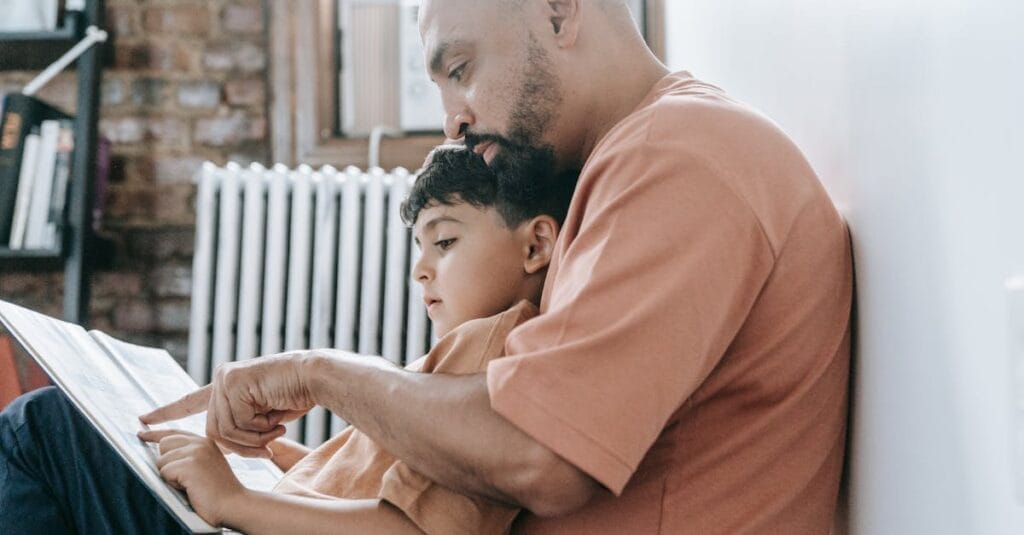 A father teaches his son to read, creating a warm bonding moment in a cozy home setting.