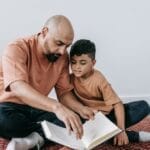 A father and son sitting on a rug, bonding over reading indoors.